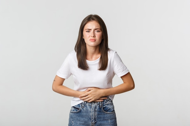 Mujer que tiene dolor de estómago, agacharse y tomarse de las manos sobre el vientre, malestar por cólicos menstruales. Chica con náuseas.