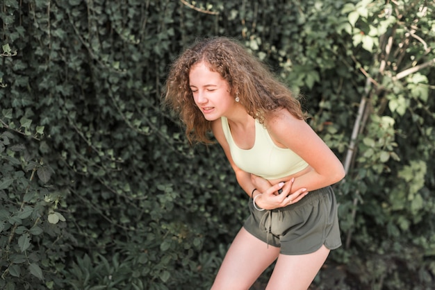 Foto mujer que tiene dolor en el estómago contra el seto