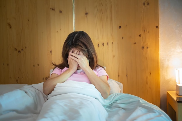 Foto mujer que tiene dolores de cabeza por migraña mientras está acostada en la cama en casa, insomnio, insomnio, sufrimiento cansado y conceptos estresados