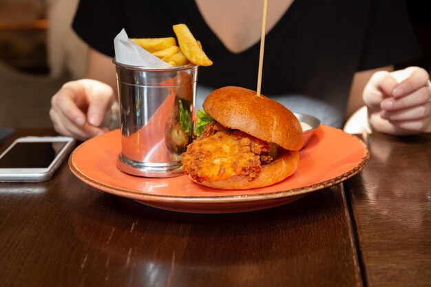 Mujer que tiene una hamburguesa crujiente deliciosa del pollo con la viruta a la hora del almuerzo.