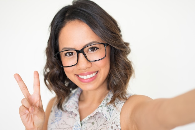 Mujer que toma la foto de Selfie y que muestra la muestra de la victoria