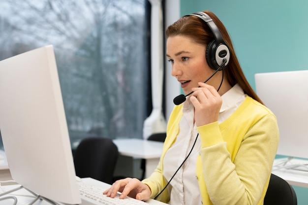 Mujer que trabaja en un centro de llamadas hablando con clientes usando auriculares y micrófono