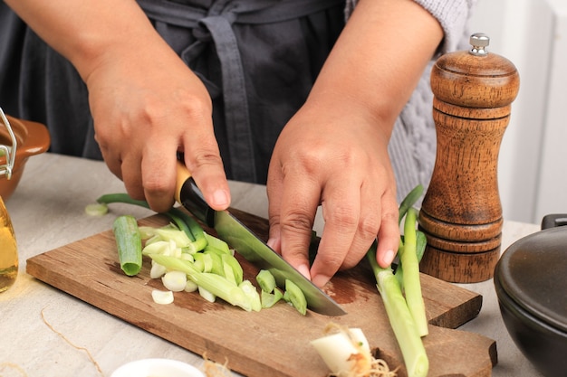 Mujer que trabaja en la cocina cortando las verduras. Mujer rebanar cebolletas para ensalada. Cerrar cebollas de corte de chef.