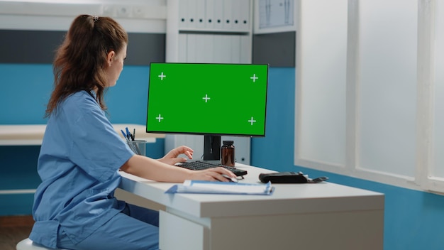 Mujer que trabaja como enfermera con pantalla verde en la computadora. Especialista en atención médica que usa monitor y teclado para clave de croma horizontal con plantilla de maqueta y fondo aislado. Sistema médico