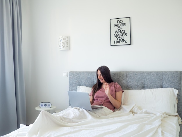 Mujer que trabaja con la computadora portátil en la cama