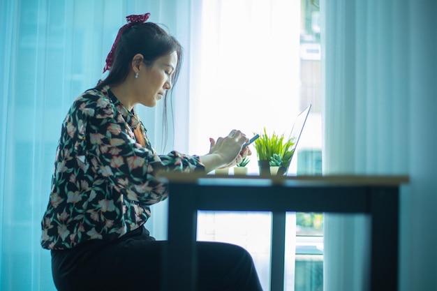 Mujer que trabaja en la computadora portátil en casa mientras habla por teléfono