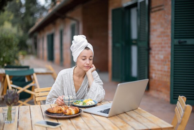 Mujer que trabaja en la computadora portátil durante el desayuno en el jardín