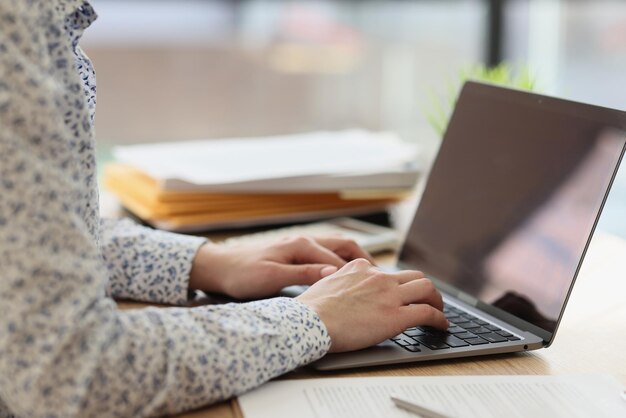 Mujer que trabaja con una computadora portátil mientras está sentada en el administrador de la mesa escribiendo en el teclado de la computadora