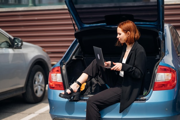 Mujer que trabaja en la computadora portátil mientras está sentado en el maletero del coche