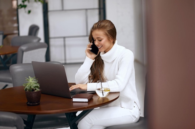 Mujer que trabaja en la computadora portátil mientras habla por teléfono