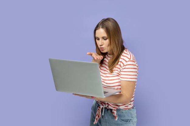 Mujer que trabaja en una computadora portátil mirando la pantalla con una videollamada que envía besos al aire