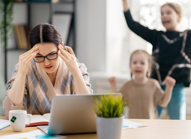 Foto mujer que trabaja en una computadora portátil. niños ruidosos y trabajo remoto desde casa.