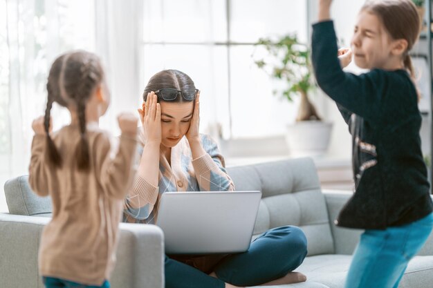 Foto mujer que trabaja en una computadora portátil. niños ruidosos y trabajo remoto desde casa.