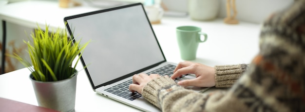 Una mujer que trabaja en la computadora portátil de pantalla en blanco con taza de café y decoración en mesa de trabajo simple