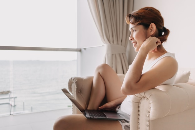 Mujer que trabaja con la computadora portátil y relajarse en el sofá del hotel