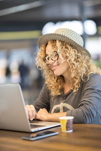 Una mujer que trabaja en una computadora portátil sentada en la mesa del bar usando conexión wifi gratuita Nómada digital y lugar de trabajo de oficina alternativo para viajeros modernos Gente de estilo de vida con concepto de trabajo inteligente