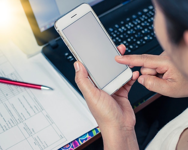 Mujer que trabaja en un escritorio de oficina y mensajes de texto con su teléfono móvil