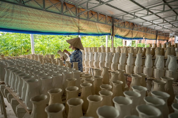 Mujer que trabaja en la fábrica de cerámica Una pila de pequeñas copas de cerámica en bruto en el estante Molde de taza de cerámica Proceso tradicional de fabricación de tazas de cerámica en la fábrica