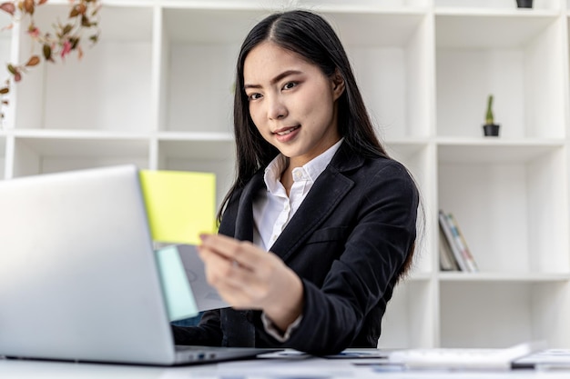 Mujer que trabaja en una oficina privada, una mujer de negocios propietaria de una empresa que sostiene un bloc de notas con notas en su computadora portátil, ella está revisando los documentos financieros de la empresa. concepto de gestión financiera de la empresa.