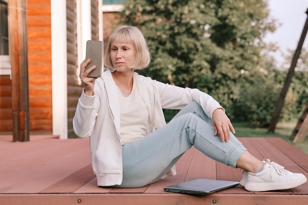 Mujer que trabaja en el parque con teléfono y computadora portátil.