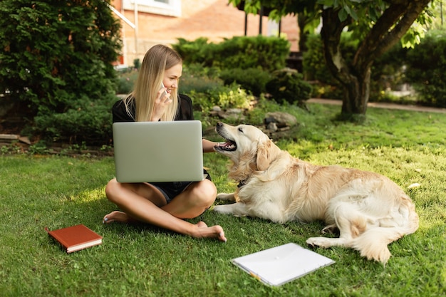 Foto mujer que trabaja con el portátil y jugando con el perro labrador en el parque