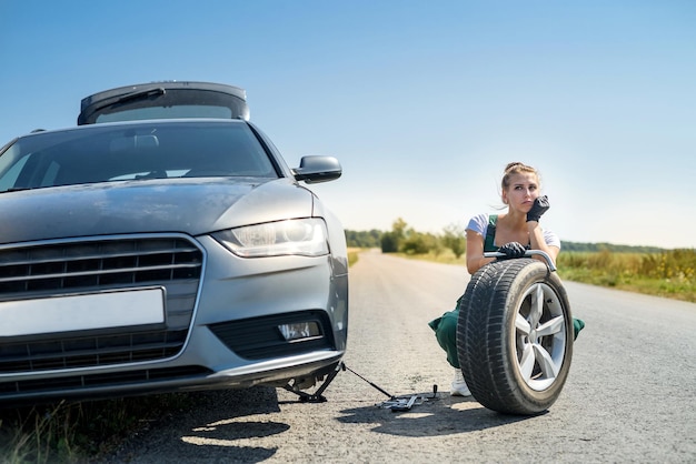 Mujer que trabaja con la rueda rota de su coche, esperando ayuda