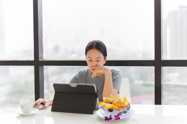 Mujer que trabaja en su computadora portátil con un plato de fruta fresca en la oficina