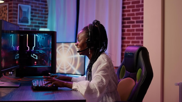 Mujer que transmite un juego de acción de disparos en primera persona en línea sorprendida después de ganar la competencia en línea en la PC de juegos. La jugadora afroamericana no puede creer el éxito en el torneo de disparos en primera persona.