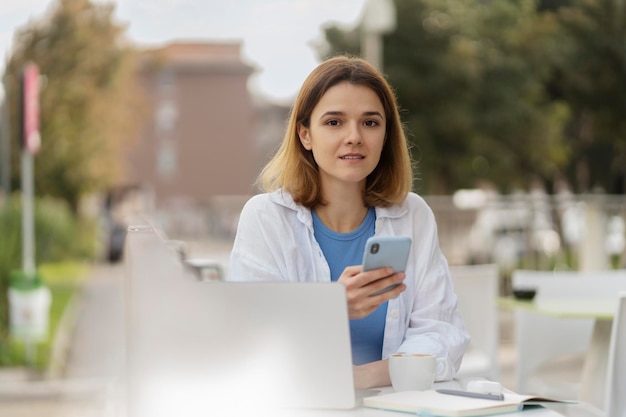 Mujer que usa la aplicación móvil mirando la cámara sentada en la calle. concepto de tecnología