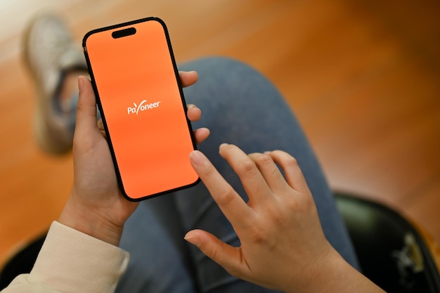 Una mujer que usa la aplicación Payoneer en su teléfono iPhone con el logotipo de Payoneer en la pantalla