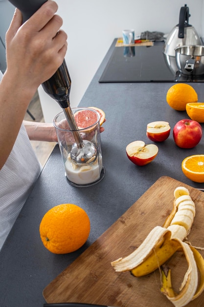 Foto mujer que usa una batidora de mano para mezclar frutas frescas en la cocina