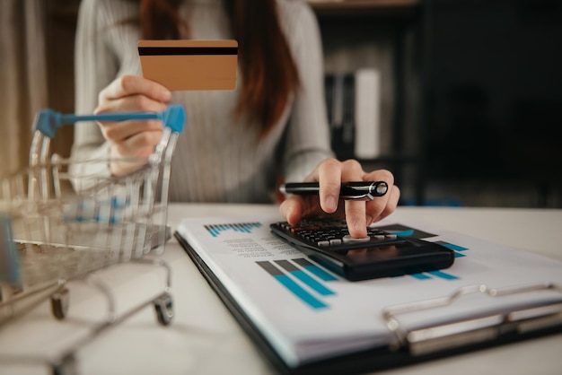 Mujer que usa el cálculo en la calculadora con los gastos del hogar y la deuda mensual de la tarjeta de crédito