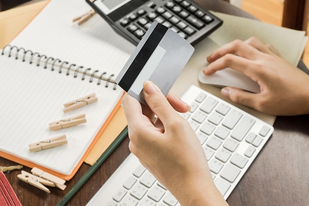 mujer que usa la computadora para comprar en línea y pagar con tarjeta de crédito, poca luz, enfoque selectivo en la mano