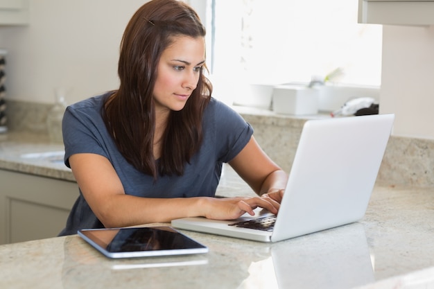 Mujer que usa la computadora portátil al lado de la PC de la tableta