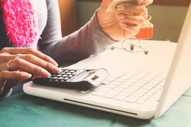 Mujer que usa la computadora portátil y la calculadora, sosteniendo la tarjeta de crédito para las compras en línea.