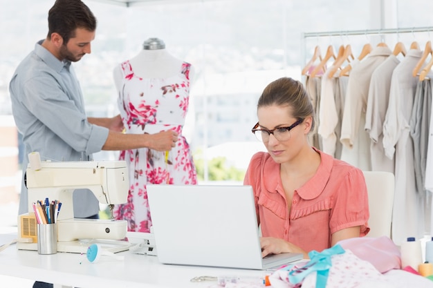 Mujer que usa la computadora portátil con el diseñador de moda que trabaja en el estudio