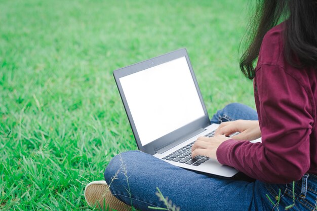 Mujer que usa la computadora portátil en fondo verde del campo