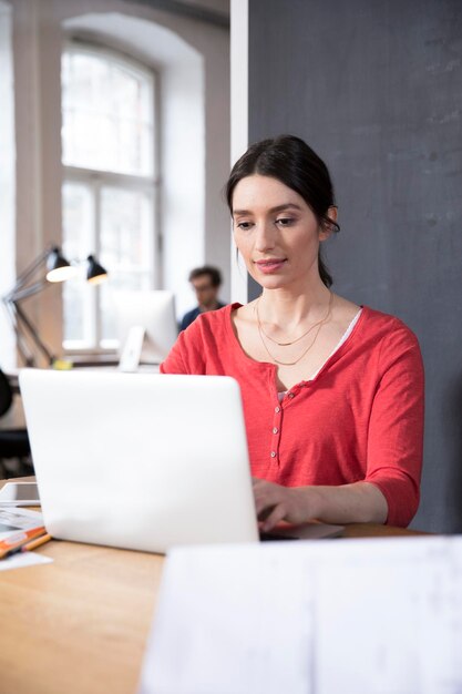 Mujer que usa la computadora portátil en la mesa en la oficina