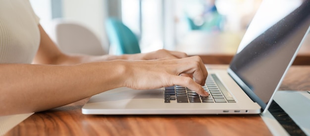 Mujer que usa una computadora portátil mujer independiente escribiendo teclado computadora portátil en un café o en una oficina moderna tecnología digital en línea y concepto de red