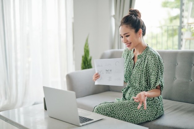 mujer que usa una computadora portátil o una tableta para chatear en línea, navegar o transmitir películas sentada en el sofá