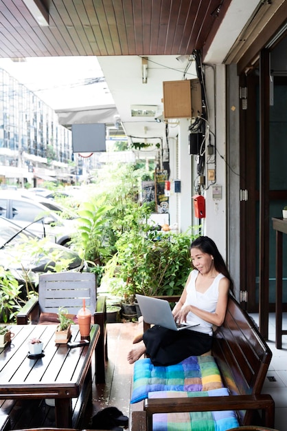 Mujer que usa la computadora portátil que se sienta en banco de la terraza