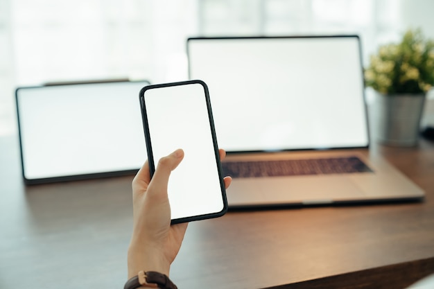 Mujer que usa la computadora portátil y la tableta digitales con smartphone en la tabla en casa. Pantalla en blanco para publicidad