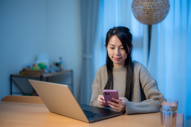 Mujer que usa una computadora portátil con teléfono móvil en casa