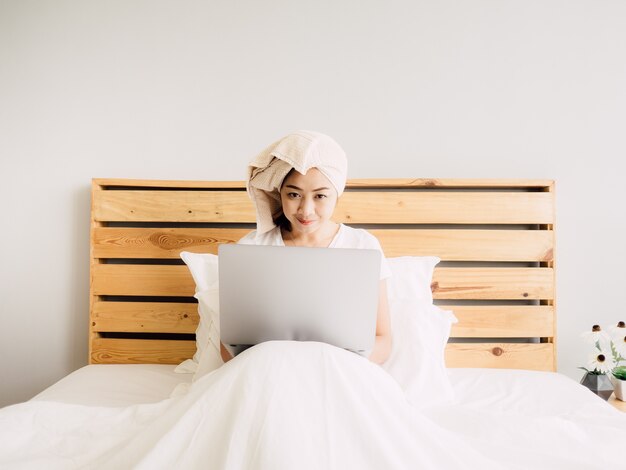 Mujer que usa la computadora en su cama en el acogedor domingo por la mañana.