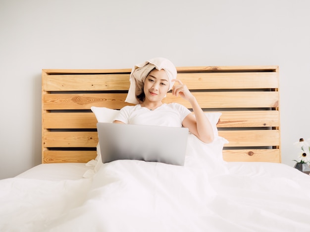 Mujer que usa la computadora en su cama en la acogedora mañana de domingo.