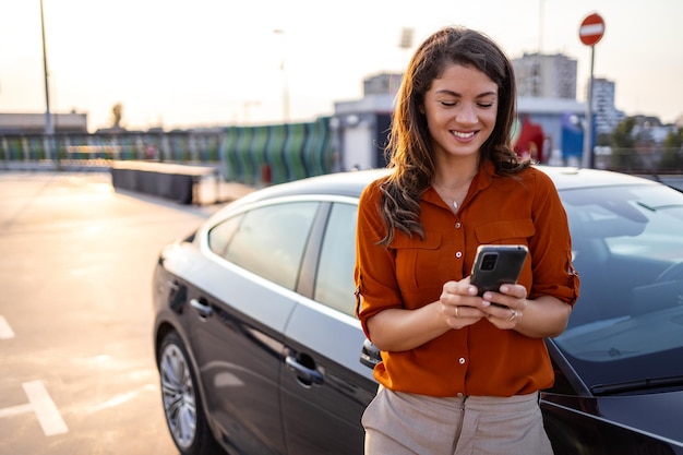 Foto mujer que usa comunicación por teléfono móvil o aplicación en línea parada cerca de un automóvil en la calle de la ciudad o estacionando al aire libre servicio de alquiler compartido de automóviles o aplicación de taxi
