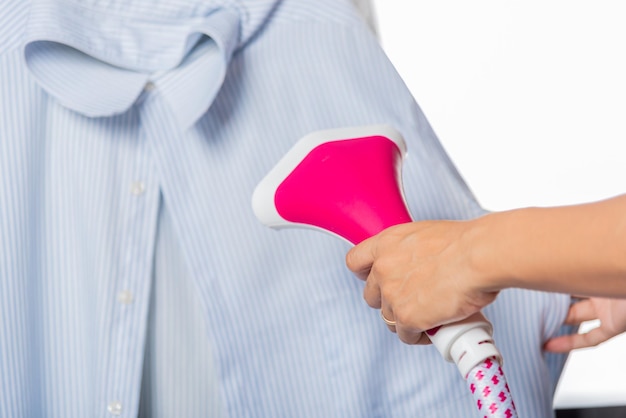 mujer que usa un generador de vapor de mano eléctrico mientras hace calor y sale vapor para la camisa de ropa