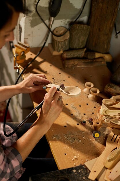 Mujer que usa herramientas eléctricas para trabajar grabadora para utensilios de madera cuchara talladora máquina de moler mientras hace artesanía Creación de recuerdos hechos a mano mujer en taller