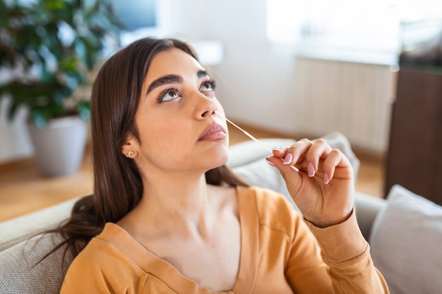 Mujer que usa un hisopo de algodón mientras realiza la prueba de PCR de coronavirus en casa. Mujer con prueba de diagnóstico rápido de coronavirus. Mujer joven en casa usando un hisopo nasal para COVID-19.