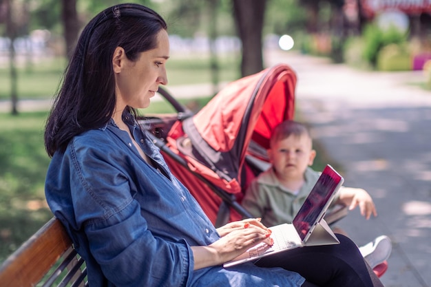 mujer que usa una laptop para trabajar mientras su hijo intenta salir del carro